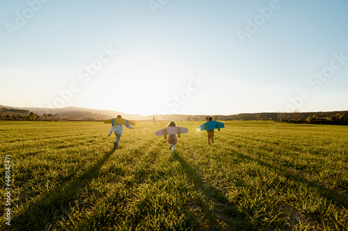 Brothers and sister with rocket wings running on agricultural field during sunny day
