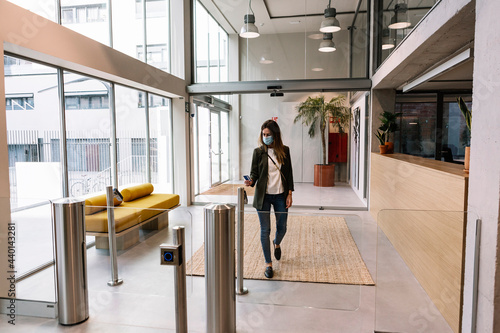 Businesswoman with protective face mask using ID card at turnstile while entering office