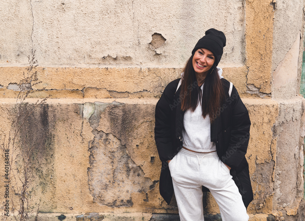 Smiling woman standing with hands in pockets in front of wall Smiling woman standing with hands in pockets in front of wall
