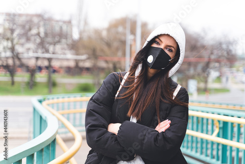 Woman wearing face mask and hooded jacket staring while standing with arms crossed