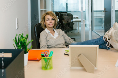 Female professional with feet up looking away while sitting at desk in office photo