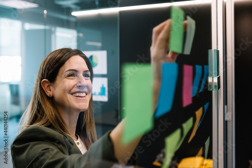 Excited businesswoman brainstorming using sticky notes on glass wall at office