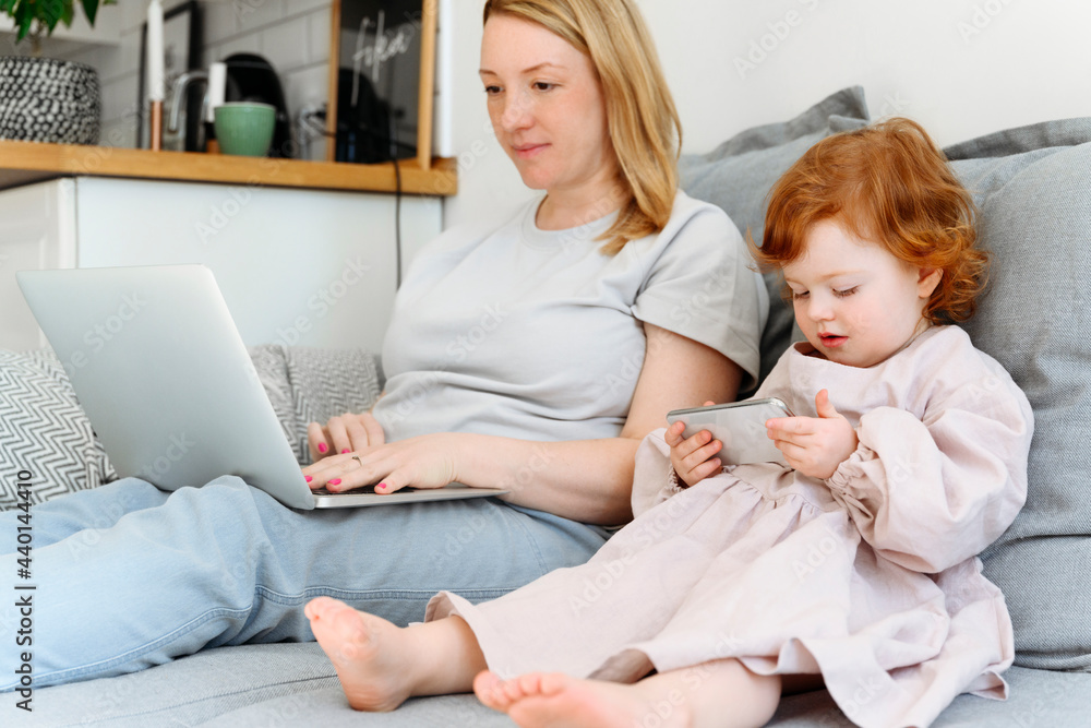 Girl using smart phone sitting by mother working on laptop at home Girl using smart phone sitting by mother working on laptop at home