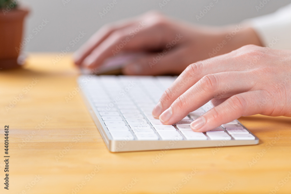 An image of a woman's hand is typing on a white keyboard on a wooden table. Selective focus An image of a woman's hand is typing on a white keyboard on a wooden table. Selective focus