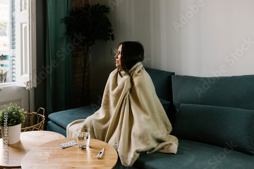 Sick woman looking away while wrapped in blanket at home photo