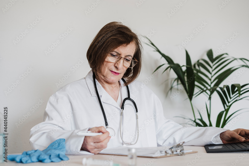 Senior female doctor reading report while sitting at desk in clinic