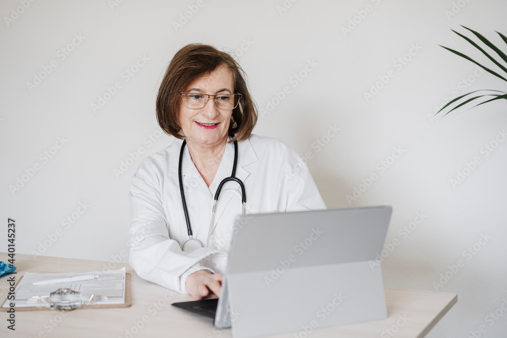 Senior doctor woman using digital tablet at desk against wall Senior doctor woman using digital tablet at desk against wall