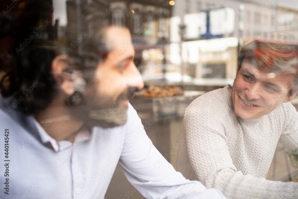 Male coworkers discussing in coworking office during coffee break seen through glass Male coworkers discussing in coworking office during coffee break seen through glass