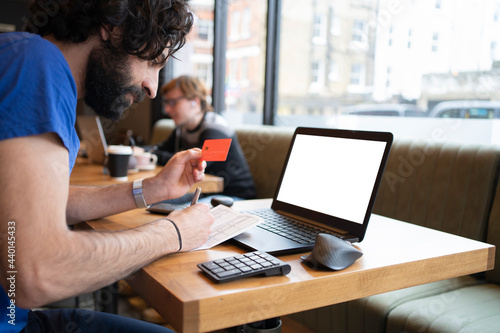 Male entrepreneur holding credit while making online payment on laptop at office photo