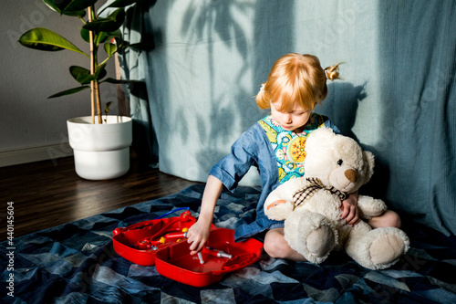 Playful blond girl aspiring doctor while holding teddy bear at home photo