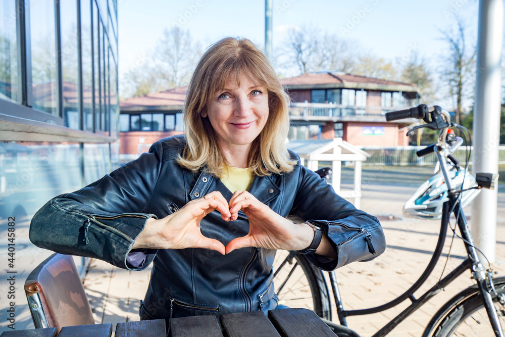 © Irina He√ü/Westend61 - Mature woman showing heart shape sign while sitting by bicycle