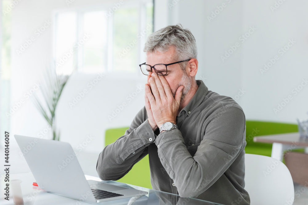 Exhausted businessman rubbing eyes at desk Exhausted businessman rubbing eyes at desk