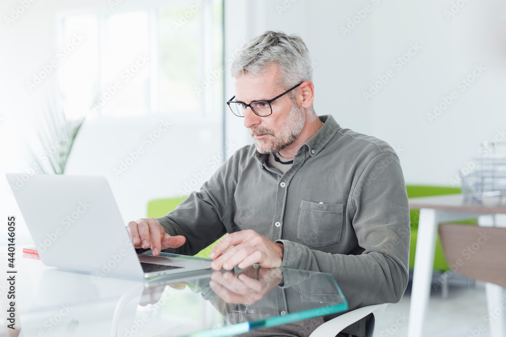 Male professional working on laptop at desk in office Male professional working on laptop at desk in office