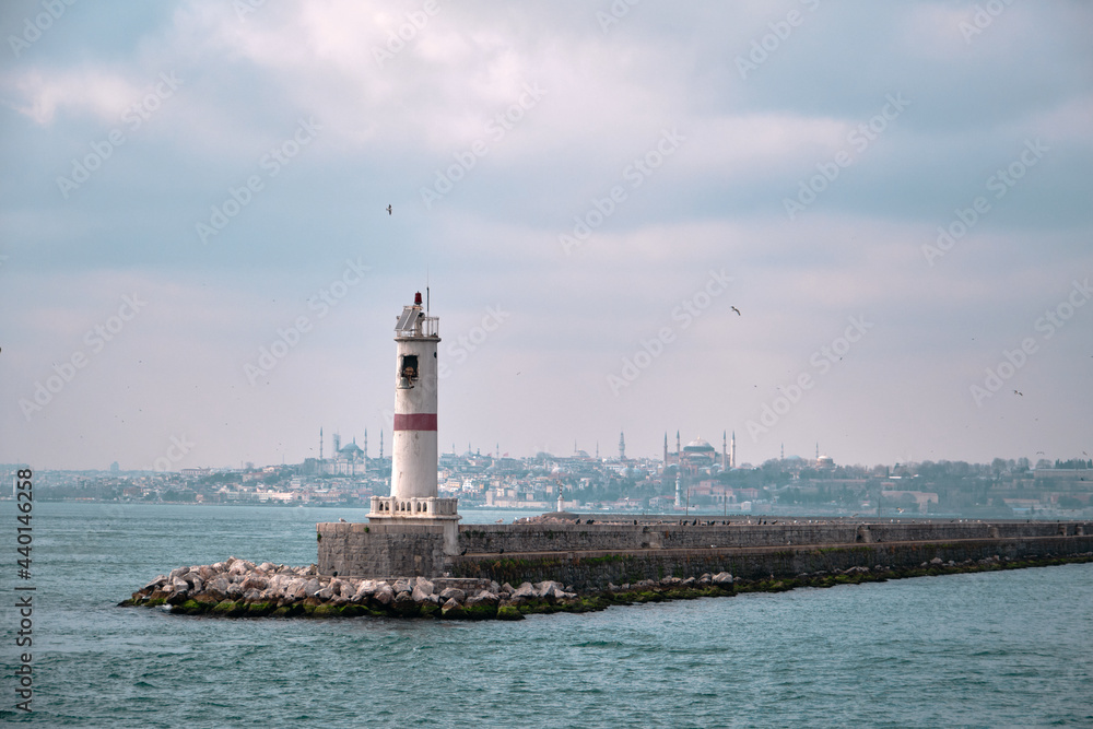 Lighthouse in bosporus with silhouette of grand ottoman mosques Hagia sophia (ayasofya) and blue (sultanahmet) mosques background with huge transportation ship sailing on the water.