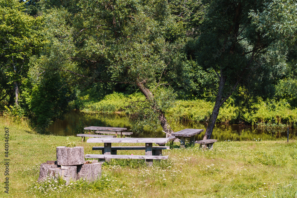 wooden benches and tables in the meadow by the river; resting place in an uncut lawn wooden benches and tables in the meadow by the river; resting place in an uncut lawn