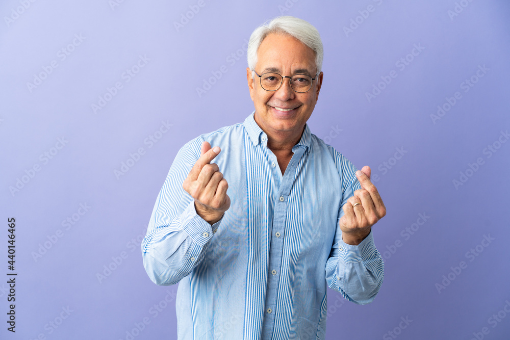 Naklejka premium Middle age Brazilian man isolated on purple background making money gesture