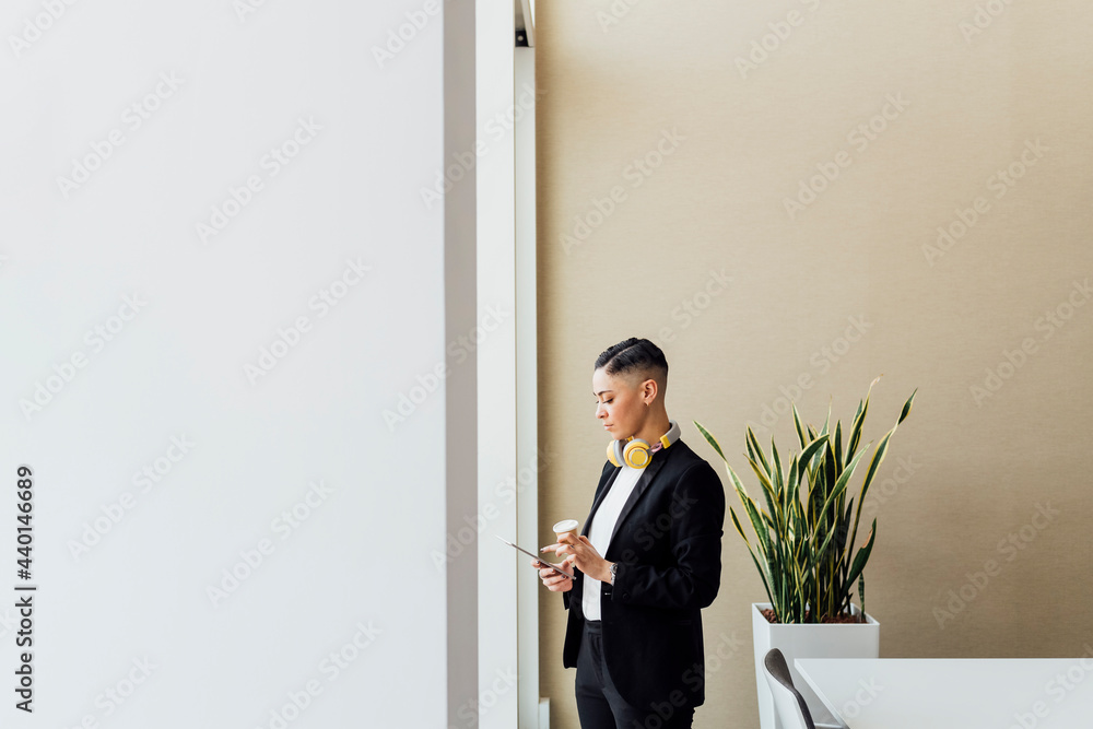 Female professional with disposable coffee cup using digital tablet in office Female professional with disposable coffee cup using digital tablet in office
