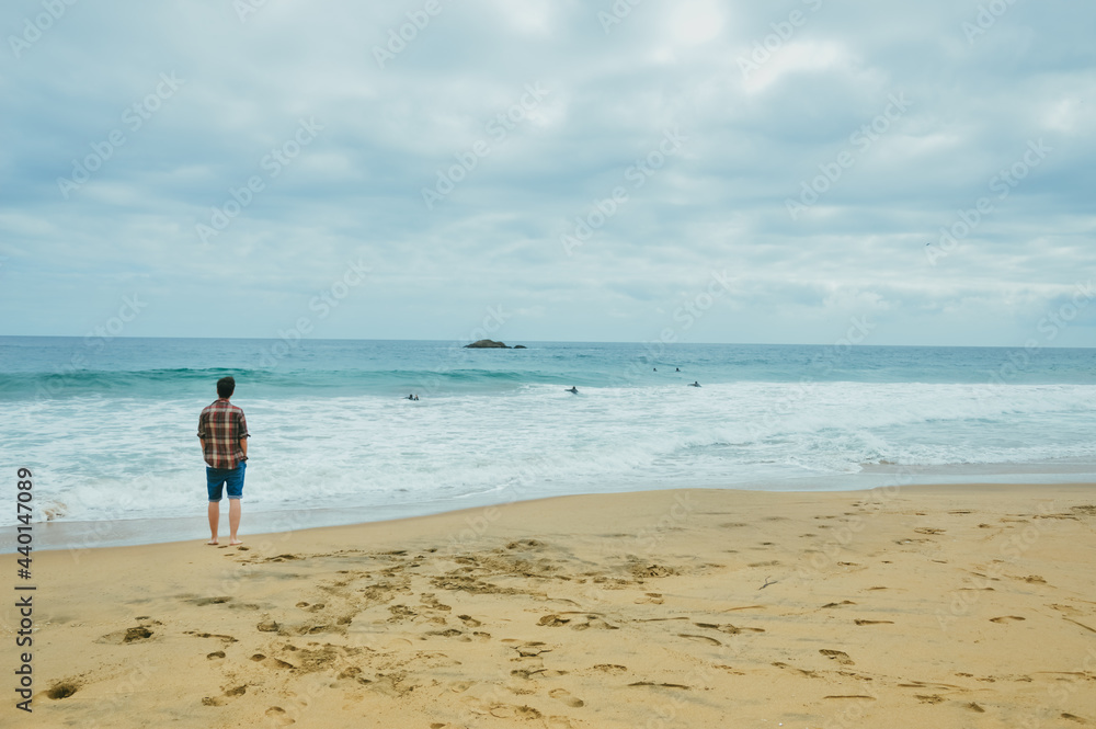 Man on the beach watches surfers