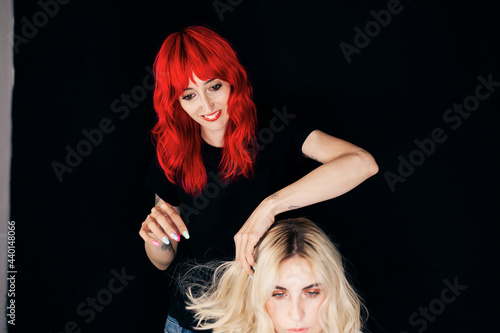 Smiling female hairstylist adjusting hair of blond fashion model in studio
