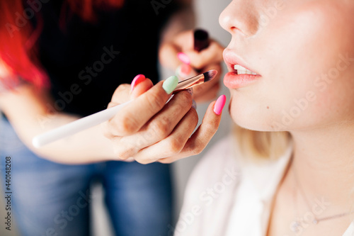 Female make-up artist applying lipstick to model in studio photo