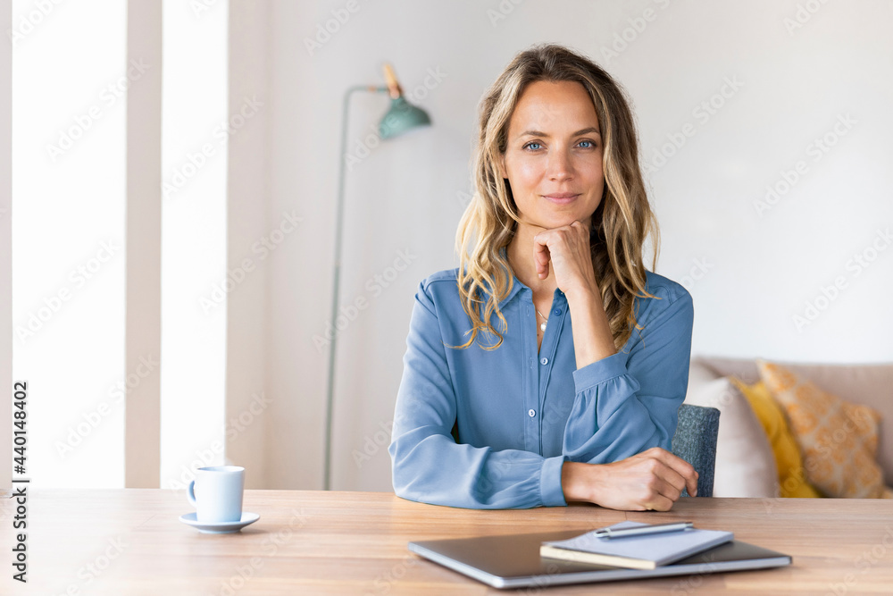 Beautiful businesswoman with hand on chin sitting at desk in home office Beautiful businesswoman with hand on chin sitting at desk in home office