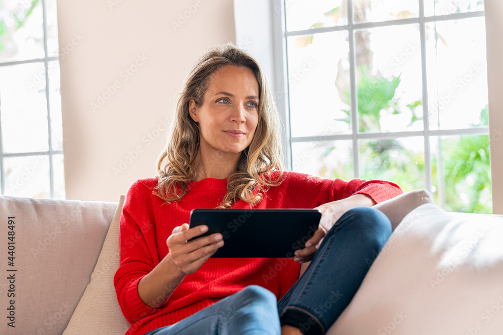 Smiling woman relaxing while holding digital tablet on couch in living room Smiling woman relaxing while holding digital tablet on couch in living room