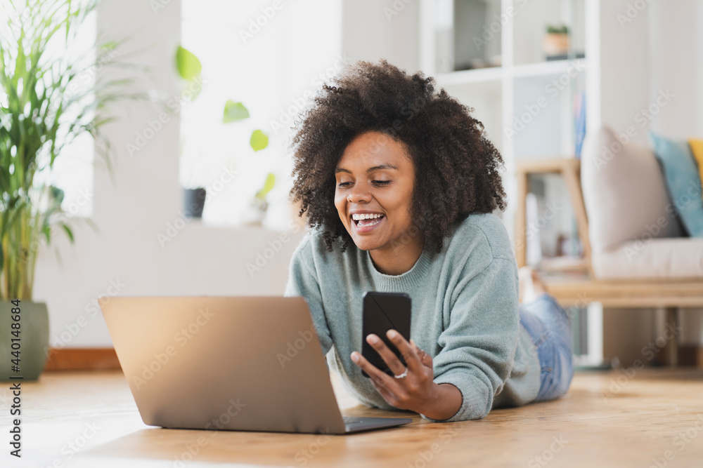 Smiling woman with mobile phone using laptop while lying on floor at home Smiling woman with mobile phone using laptop while lying on floor at home