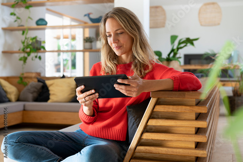 Woman using digital tablet while sitting on couch in living room