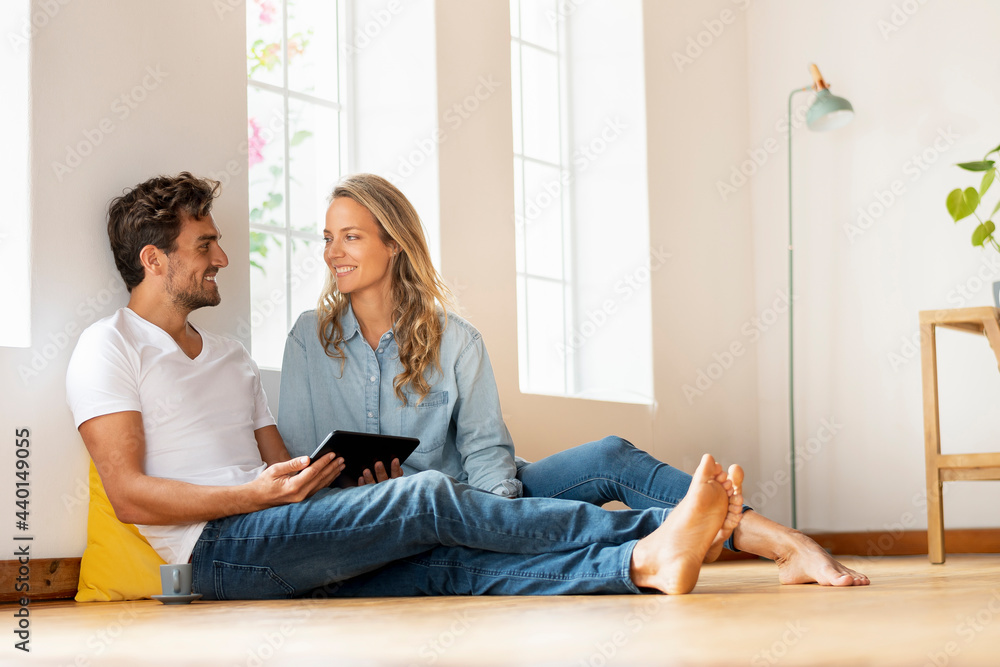 Man with digital tablet looking at girlfriend while sitting on floor at home Man with digital tablet looking at girlfriend while sitting on floor at home