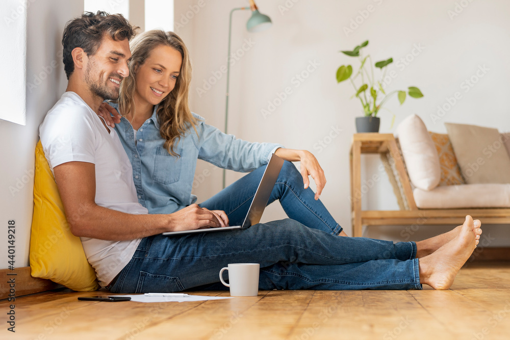 © steve brookland/Westend61 - Relaxed couple looking at laptop while sitting together at home office