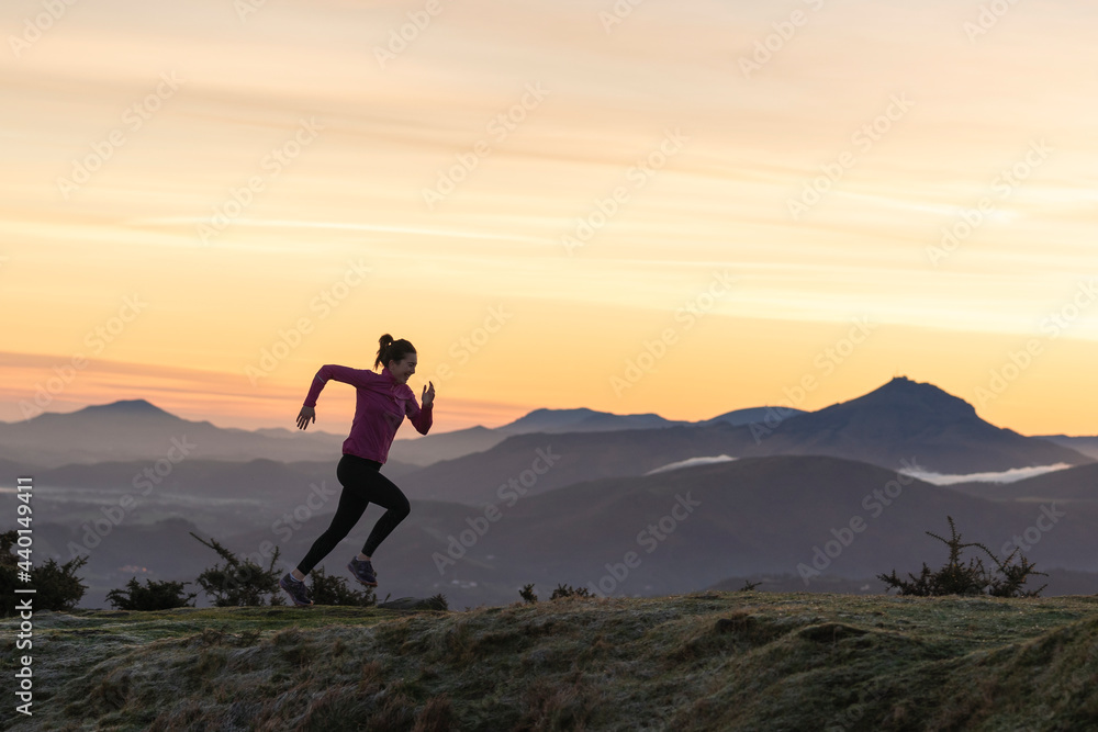 Female runner running on hill by dramatic sky Female runner running on hill by dramatic sky