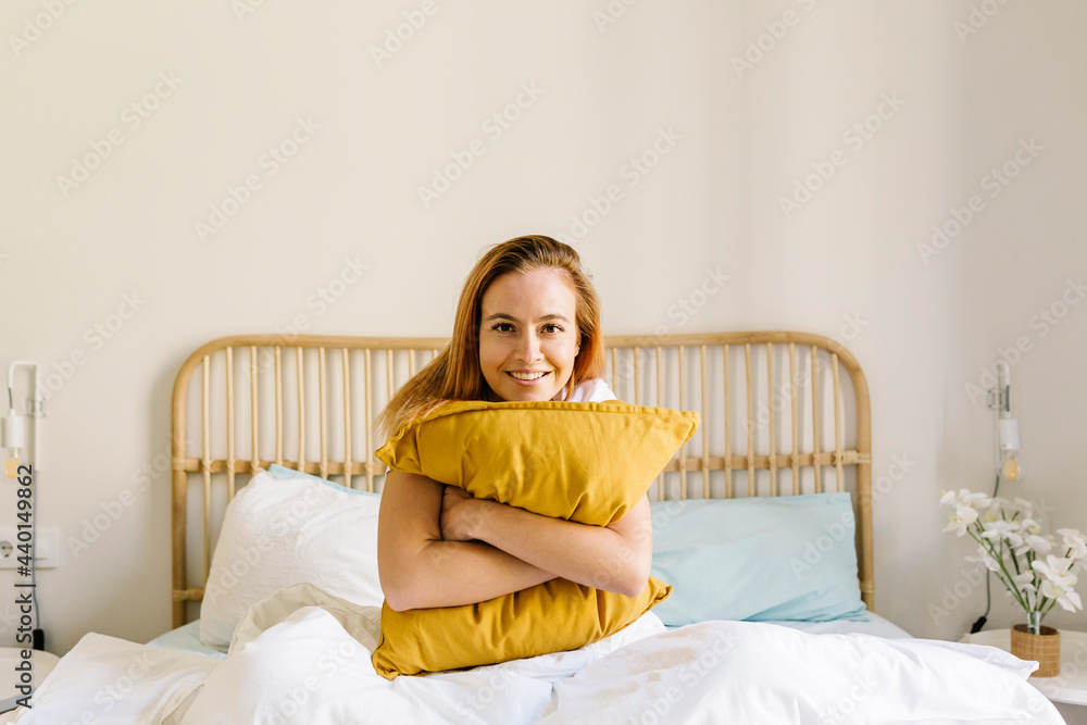 Smiling woman embracing pillow on bed at home