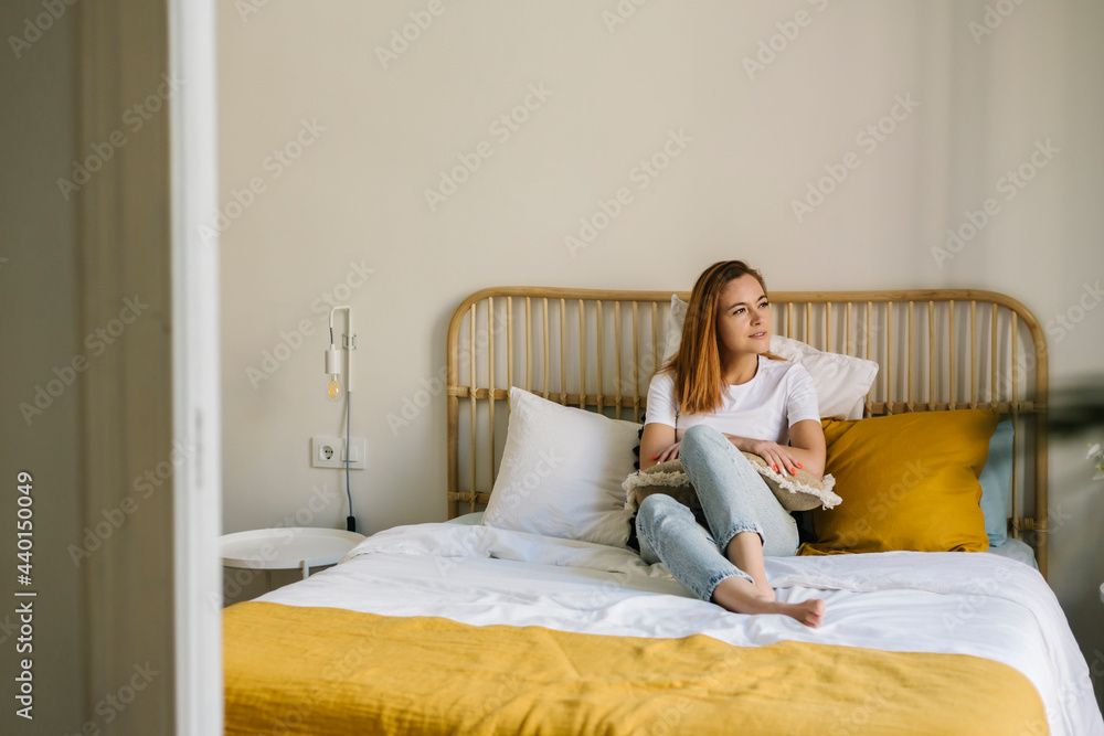 Smiling woman looking away while relaxing on bed at home Smiling woman looking away while relaxing on bed at home