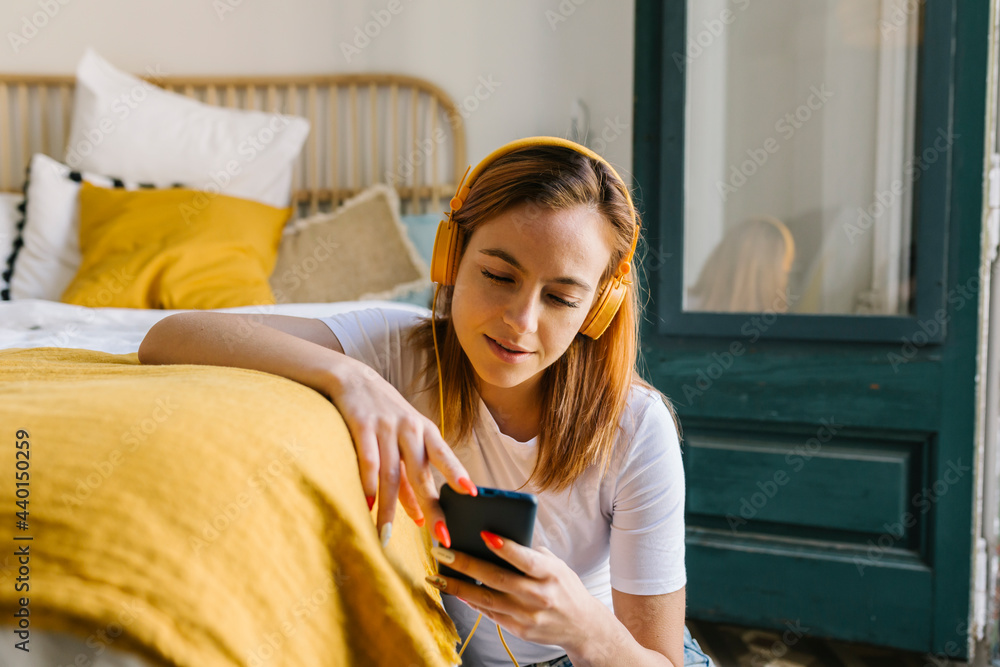 Redheaded woman using mobile phone while leaning on bed at home