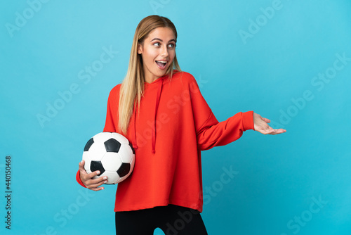 Young football player woman isolated on blue background with surprise expression while looking side