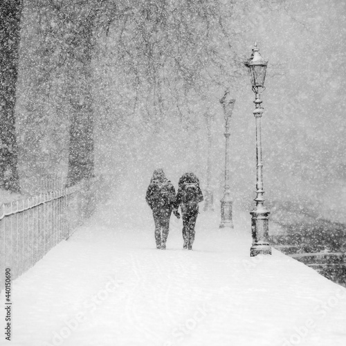 Couple walking together in snow-covered park during heavy snowfall
