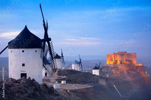 Spain, Province of Toledo, Consuegra, Historical windmills at dusk with Castle of La Muela in background photo
