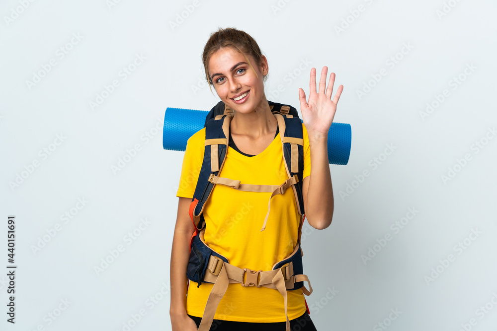 Young mountaineer woman with a big backpack isolated on white background saluting with hand with happy expression Young mountaineer woman with a big backpack isolated on white background saluting with hand with happy expression