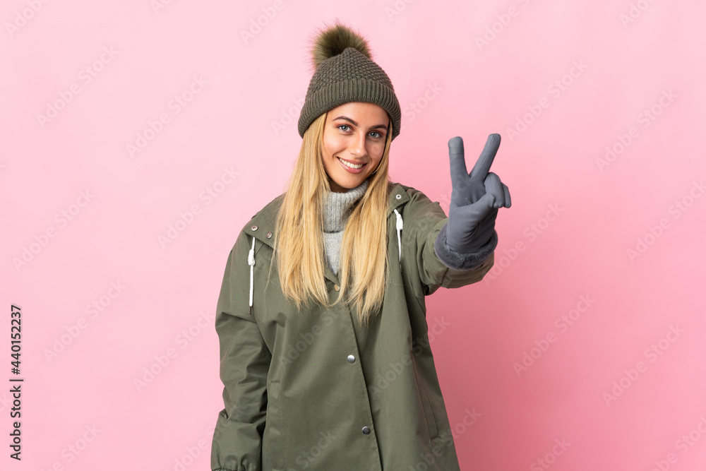 Young woman with winter hat isolated on pink background smiling and showing victory sign Young woman with winter hat isolated on pink background smiling and showing victory sign