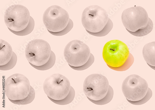 Pattern of rows of bland light pink apples with single vibrant green one