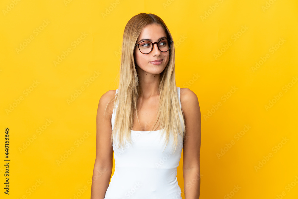 Young blonde woman isolated on yellow background having doubts while looking side Young blonde woman isolated on yellow background having doubts while looking side