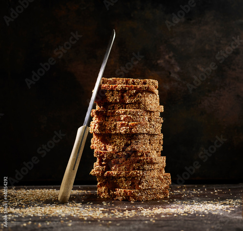 Studio shot of kitchen knife leaning on stack of fresh wholegrain bread slices photo