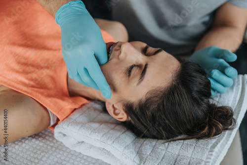 Physiotherapist giving therapy to jaw muscles of female patient in medical practice photo