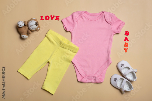 Close-up top view. Mockup blank pink bodysuit, yellow pants and white newborn sandals on a beige background, with copy space - perfect baby clothes mockup template