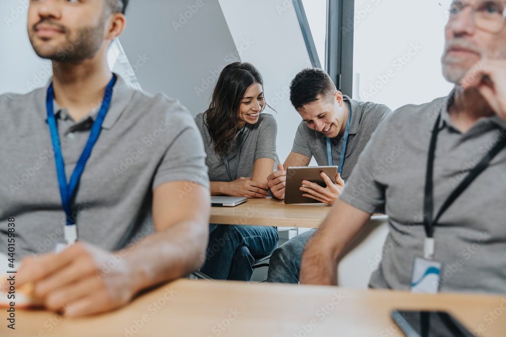 Smiling man using digital tablet by female trainee on bench in classroom Smiling man using digital tablet by female trainee on bench in classroom