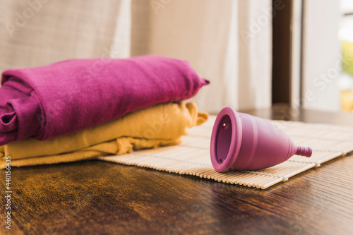 Menstrual cup on bamboo mat at table by colored clothes photo