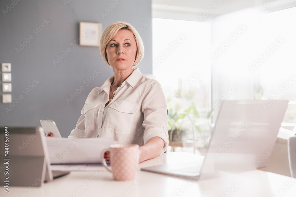Female professional with documents looking away while working in home office Female professional with documents looking away while working in home office
