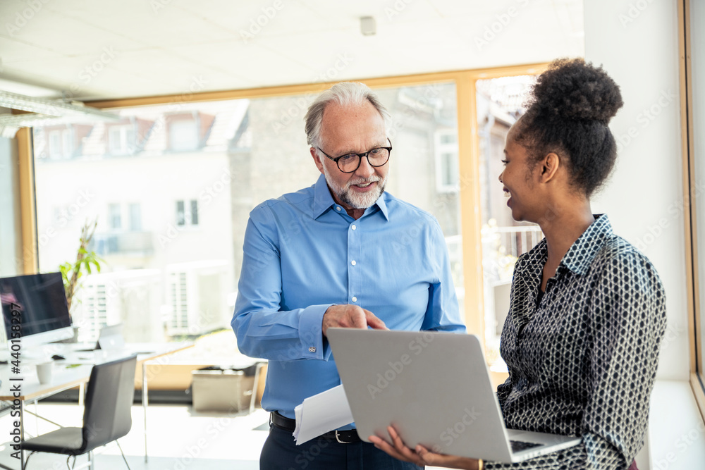 Smiling businessman discussing over laptop with female professional at office Smiling businessman discussing over laptop with female professional at office