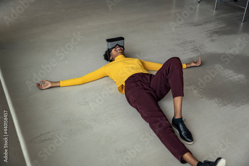 Woman wearing virtual reality headset lying on floor at office photo