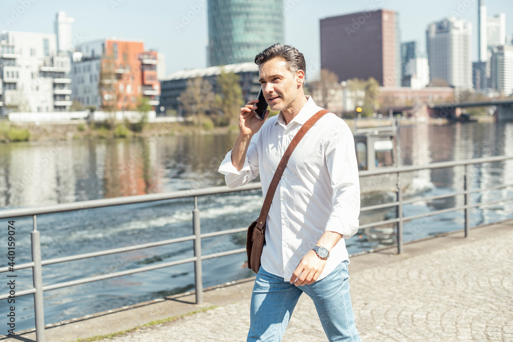 Businessman with crossbody bag talking on mobile phone during sunny day Businessman with crossbody bag talking on mobile phone during sunny day